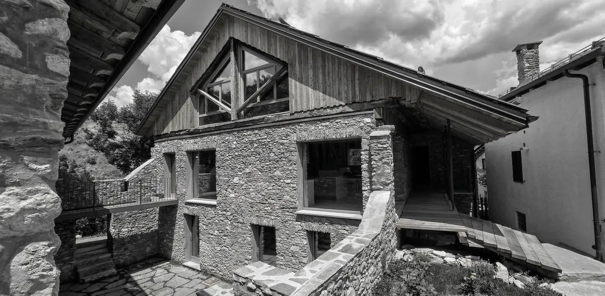 Casa di montagna in pietra con grandi serramenti in legno larice, facciata vetrata triangolare, architettura alpina