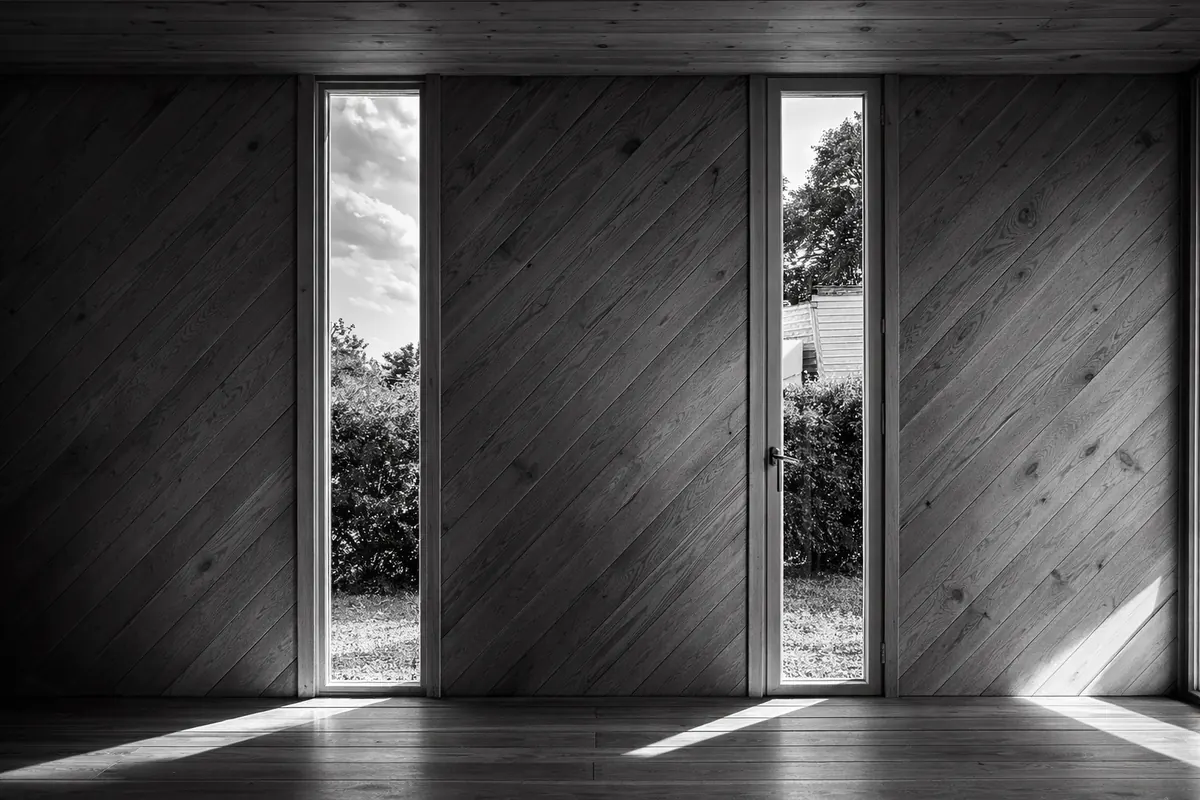 Finestre in legno minimal a fessura verticale in interno rivestito di legno diagonale, luce naturale radente