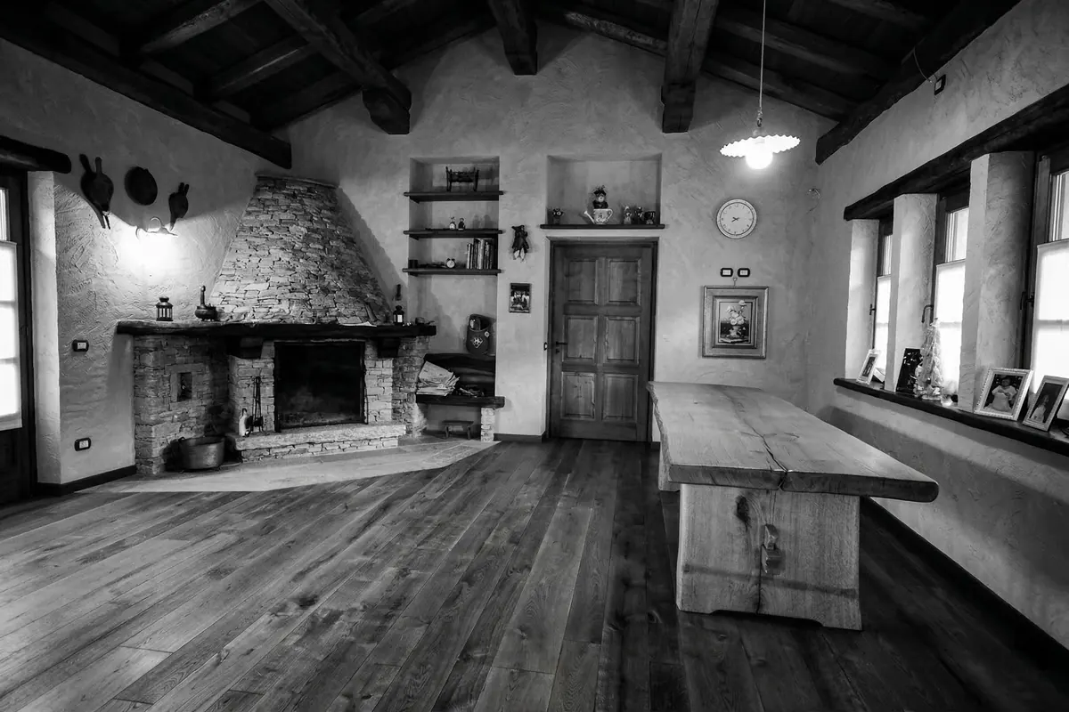 Interno di casa di montagna con tavolo in legno rustico, travi a vista, camino in pietra e pavimento in legno