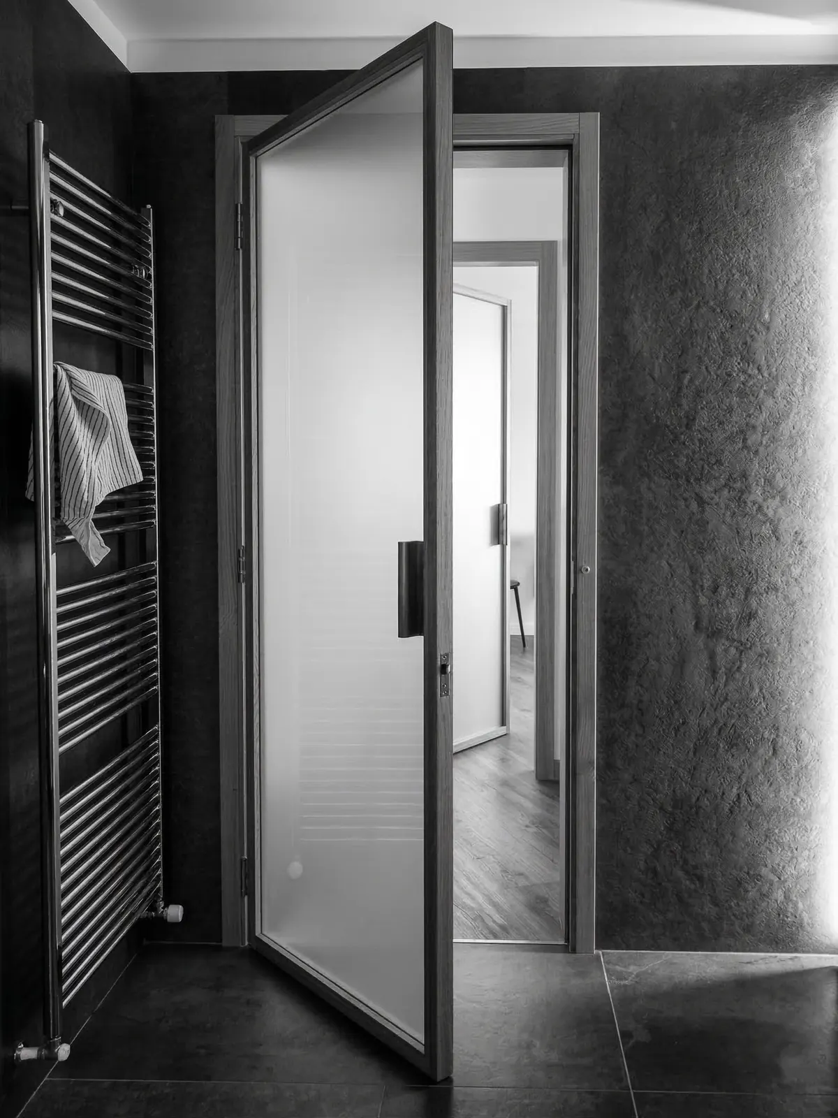 Porta pivot minimale in rovere con vetro satinato, bagno con pareti in microcemento e scaldasalviette